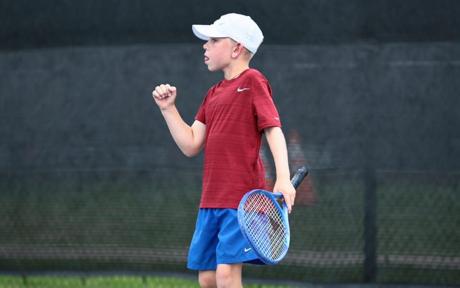 A junior player celebrating a won point, fist clenched, racquet in hand