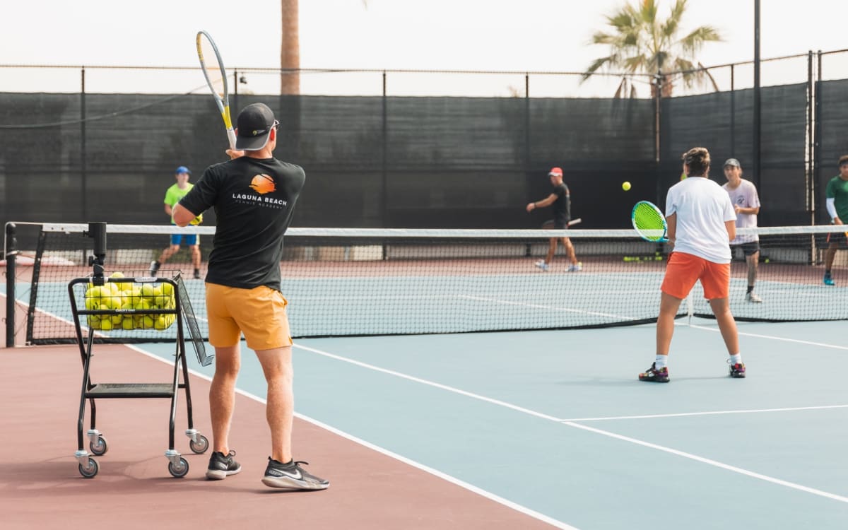 A coach feeding from a ball cart with adults spread across the court in continuous play