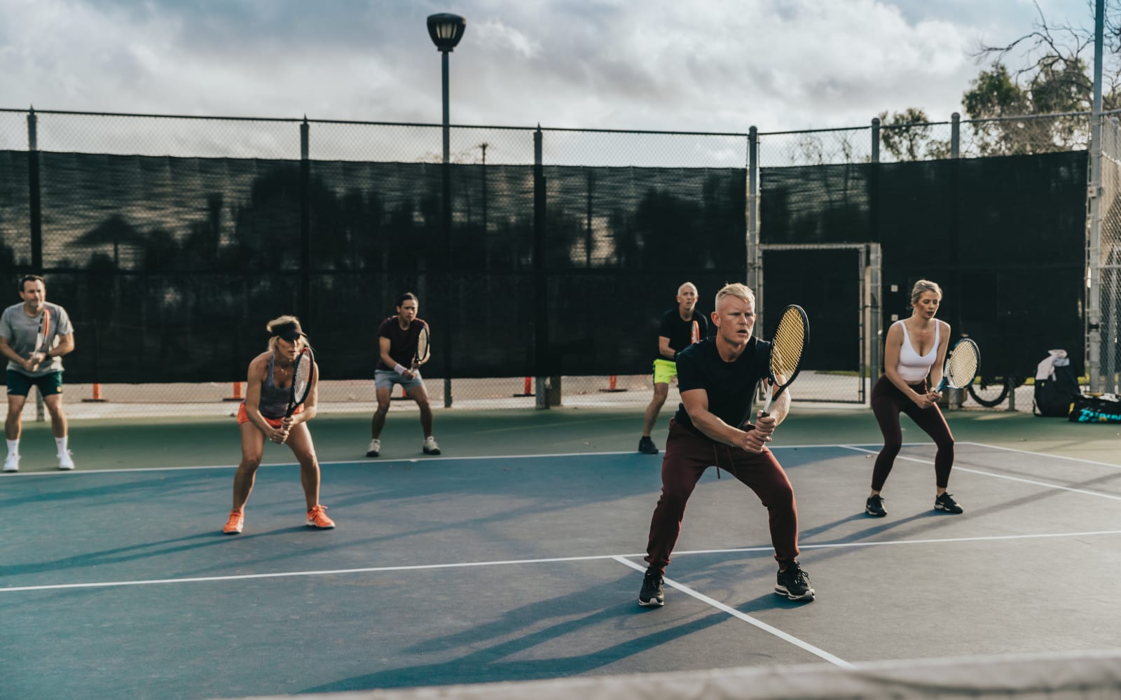 Adults spread across the court in ready position during an evening drill