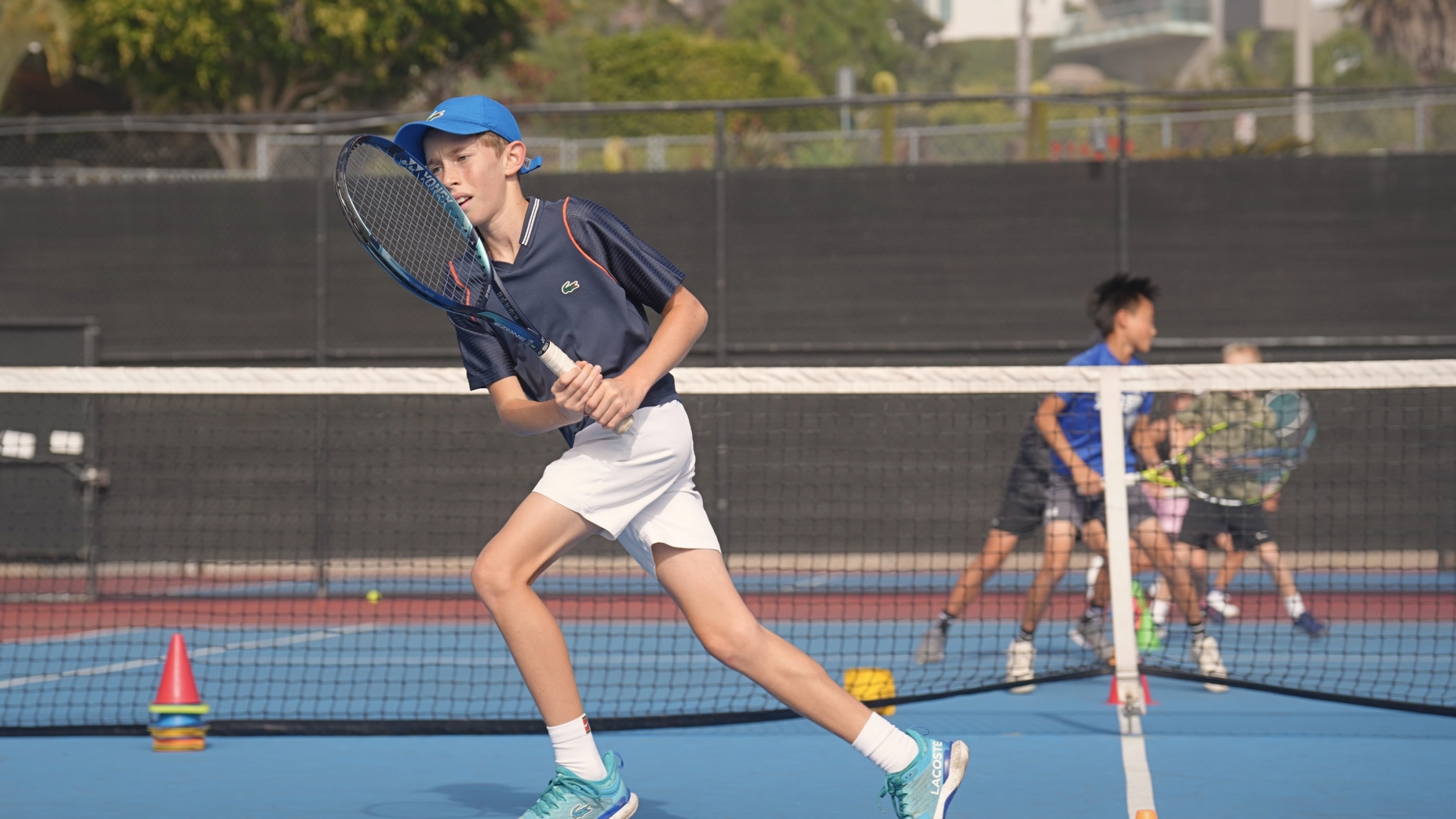 A junior driving a backhand at an LBTA camp, with the group playing behind